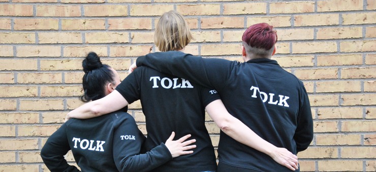 Tre tolkar som visar sina ryggar och har svarta tröjor med ordet Tolk tryckt på. 