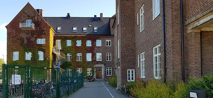 Vi finns i detta hus som är en äldre brun tegelbyggnad i tre våningar samt takvåning. Huset är i vinkel med en lång huskropp till höger, en huskropp rakt fram och en utstickande gavel till vänster.