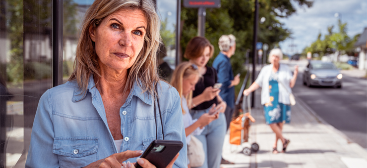 Kvinna står vid en busshållplats och håller i en mobiltelefon.