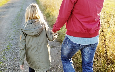 Ett barn och en vuxen håller varandra i handen och går ute i naturen.