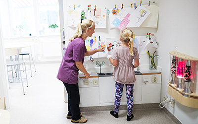 Vårdpersonal och ett barn hänger upp teckningar på väggen.