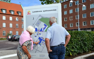 Två besökare står utanför sjukhuset och tittar på en karta över sjukhusområdet.